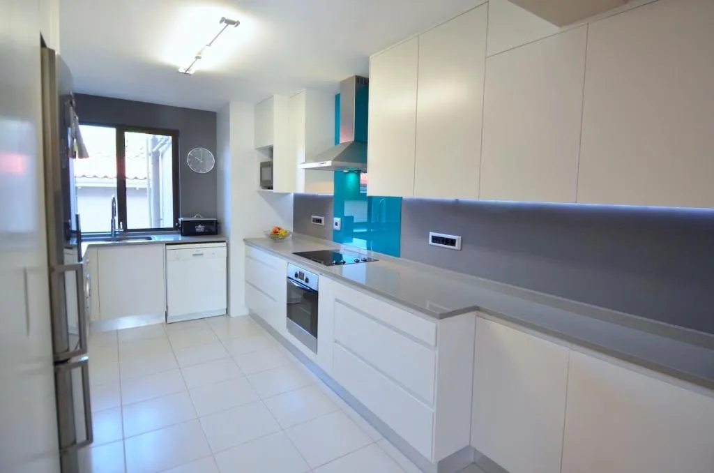 Galley kitchen with a turquoise glass splashback, gas hob and built-in oven