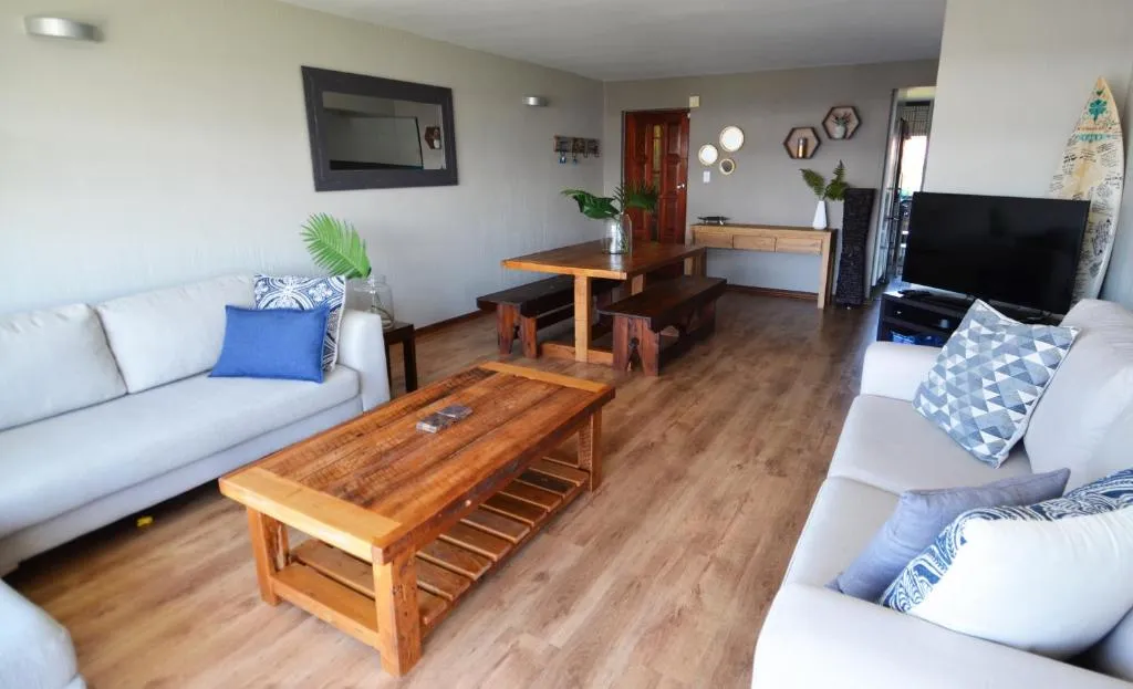Living and dining area with cream sofas, a reclaimed-wood table and a surfboard on display