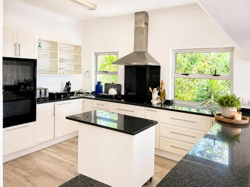 Open kitchen with white cabinetry, a central island and dual windows onto greenery