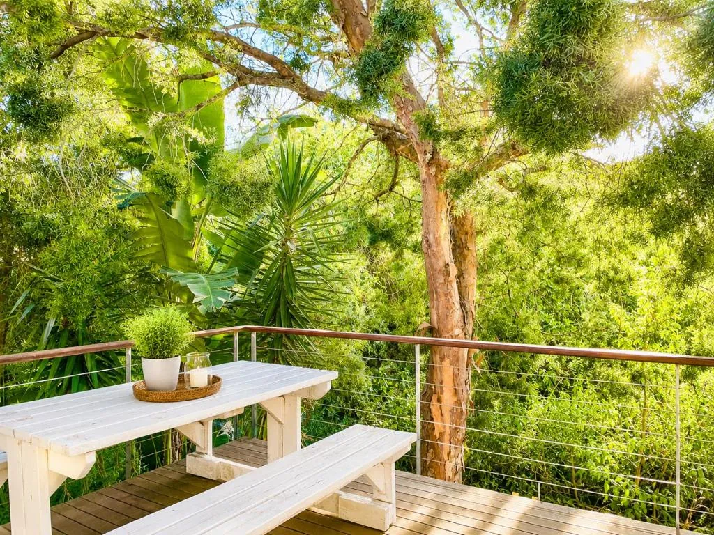 Wooden deck with a picnic table tucked beneath tree canopy and dappled light