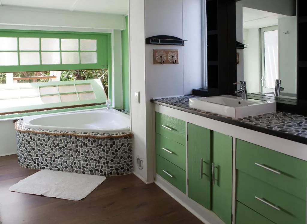 Ensuite bathroom with green cabinetry and a pebble-mosaic corner bathtub