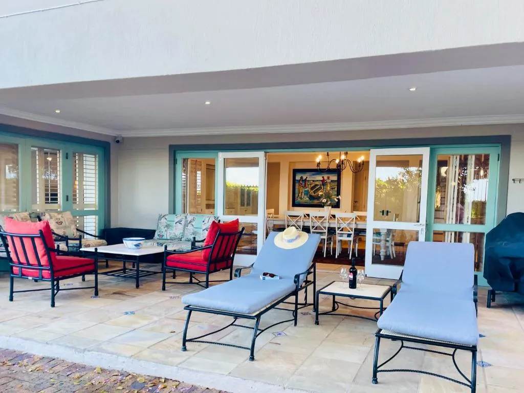 Covered patio with red-cushioned lounge chairs, sun loungers, and glass doors into the dining room