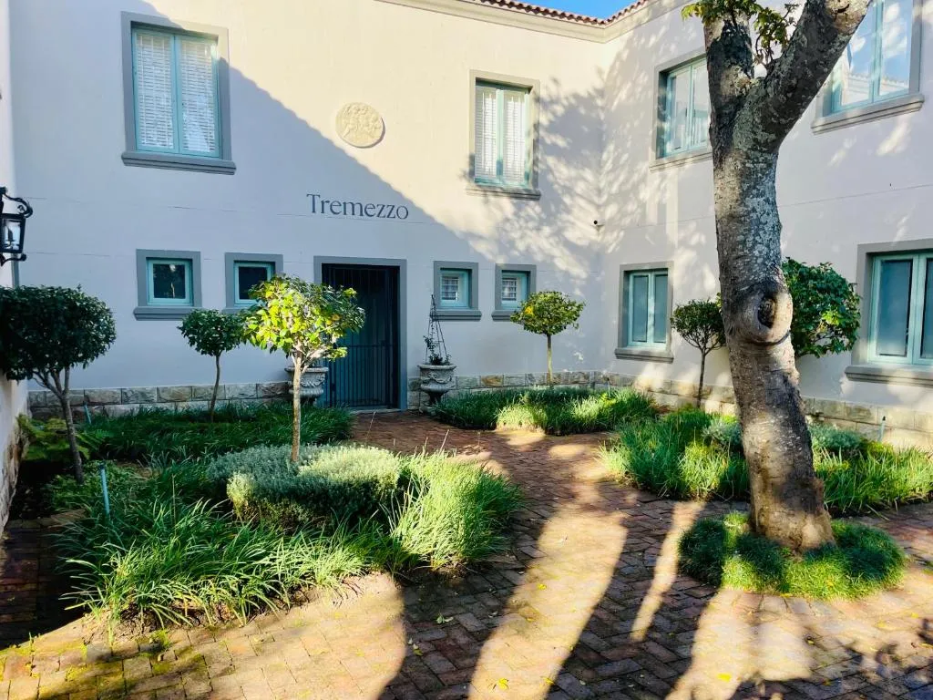 Landscaped entrance courtyard with clipped topiary, a brick path, and the villa's iron gate