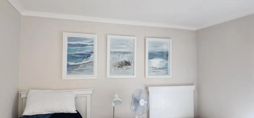 Bedroom with three framed seascape paintings above the headboard and a pedestal fan