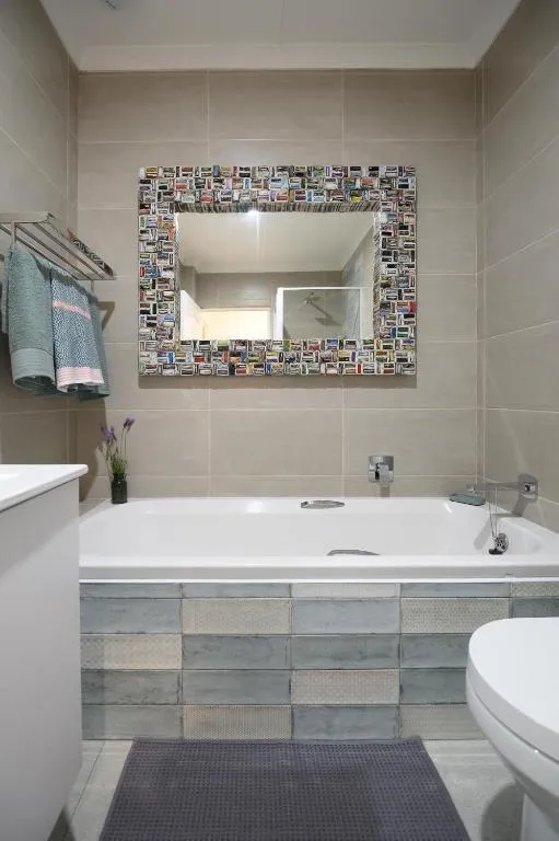 Bathroom with a mosaic-tile framed mirror over the tub and a floor-standing towel rail