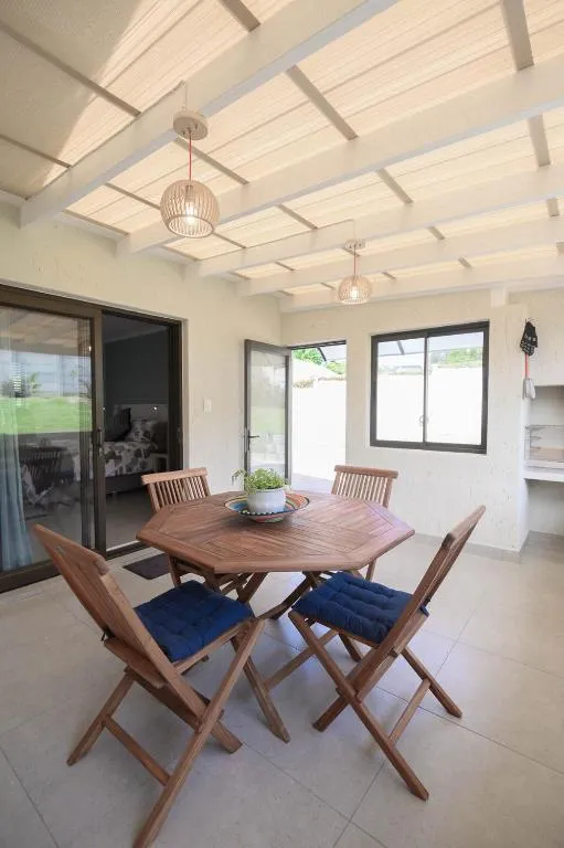 Covered pergola-roofed patio with a round wooden table, folding chairs and a built-in braai nook