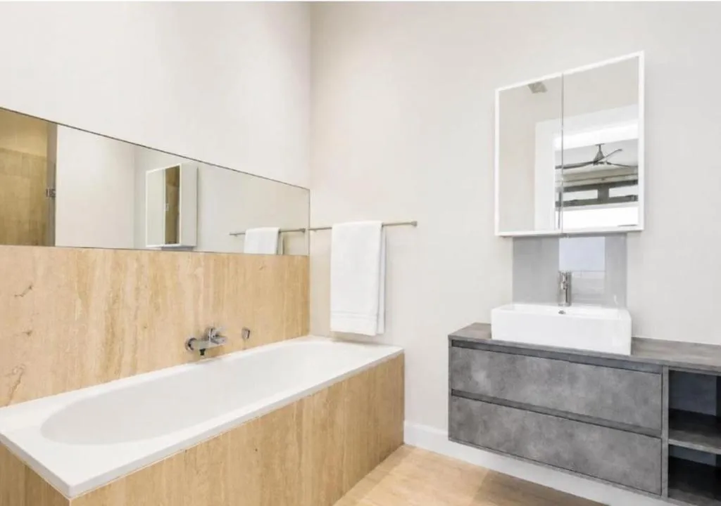Bathroom with a travertine-clad tub, floating vanity and mirrored cabinet
