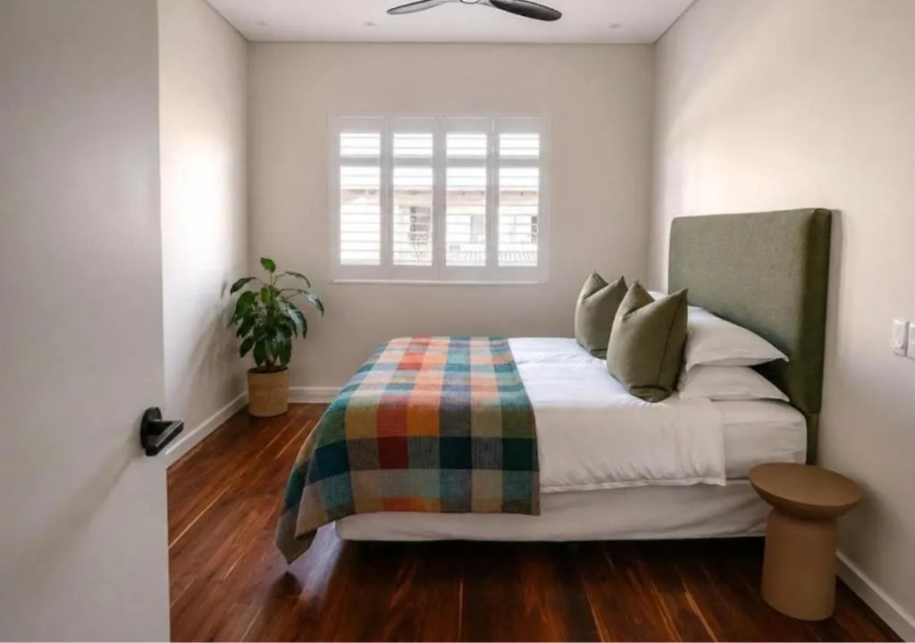Bedroom with a green upholstered headboard, plaid throw and plantation-shuttered window