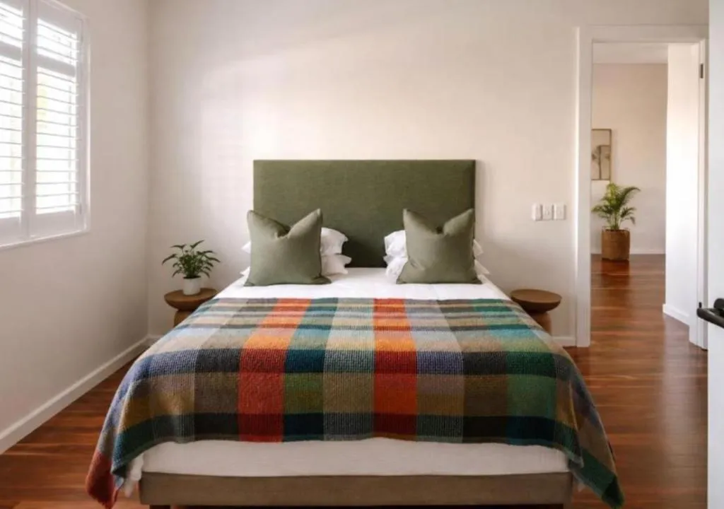 Same bedroom viewed toward the hallway, with a potted plant and wooden bedside stools