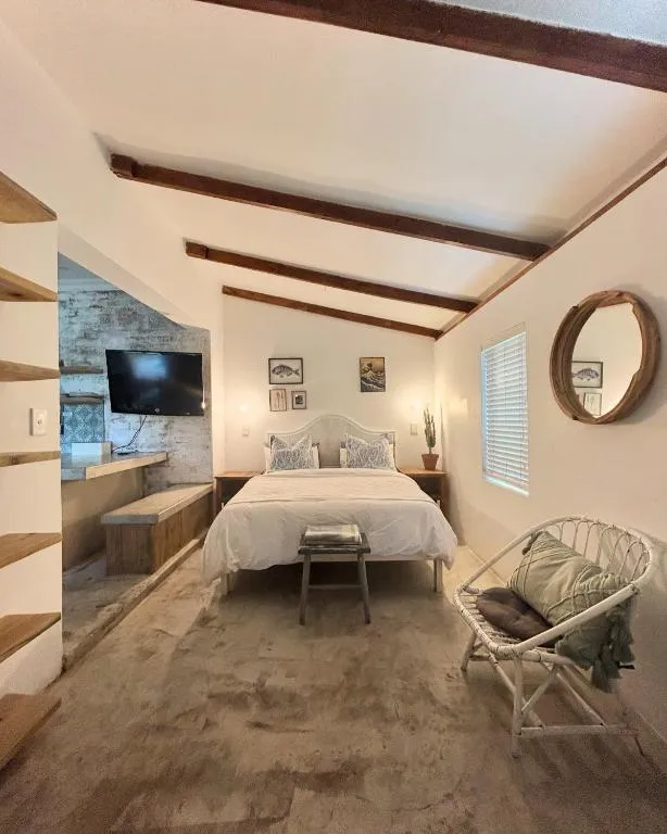 Loft bedroom with exposed timber beams, wall-mounted TV and polished concrete floor
