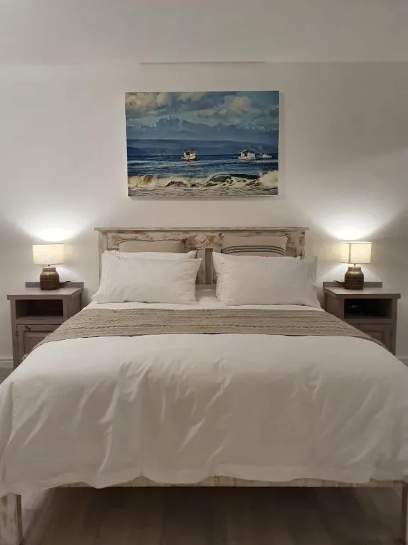 Bedroom with a whitewashed timber headboard and a framed seascape above twin bedside lamps