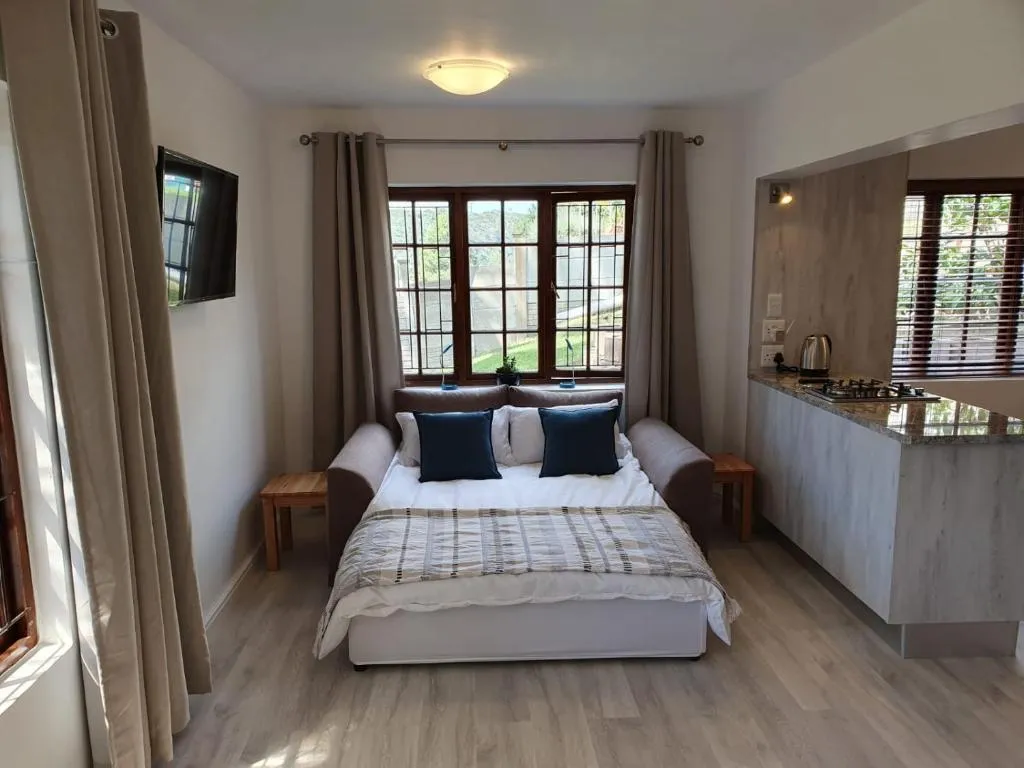 Sofa bed and kitchenette beneath a window looking onto the garden and hills