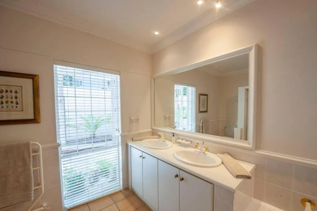 Bathroom with double vanity, gold-tone taps and louvre window to a courtyard