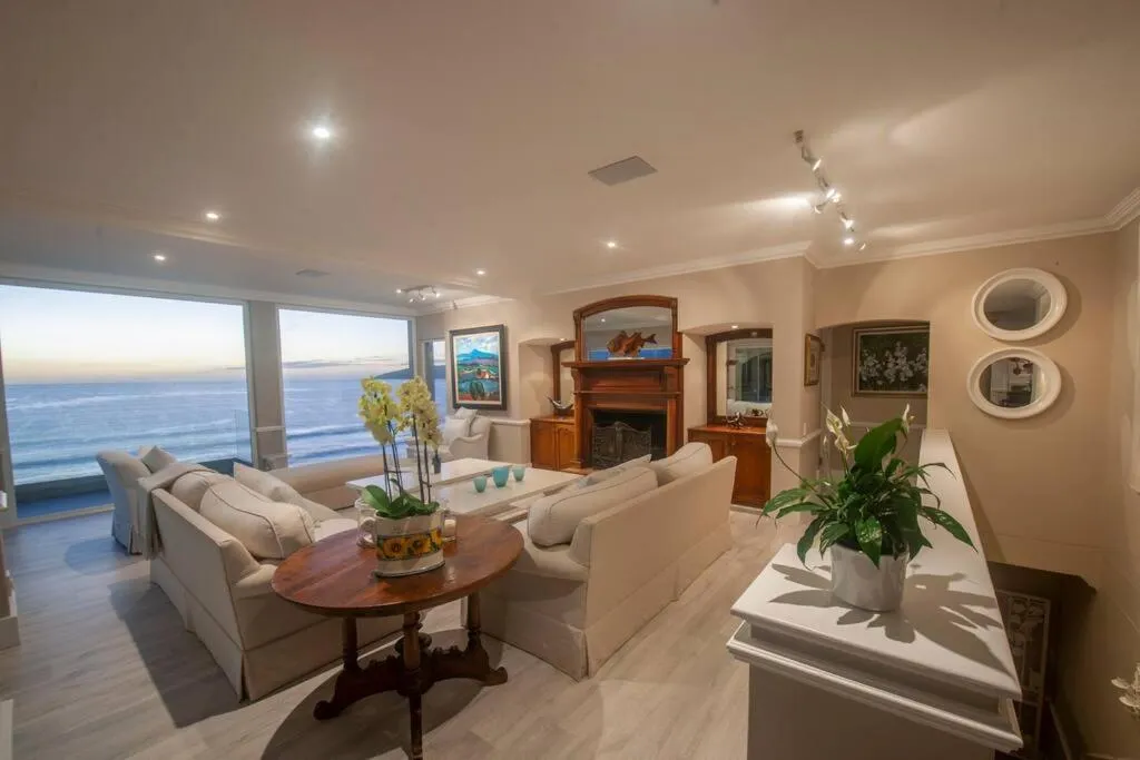 Living room with fireplace and floor-to-ceiling windows framing the ocean at dusk