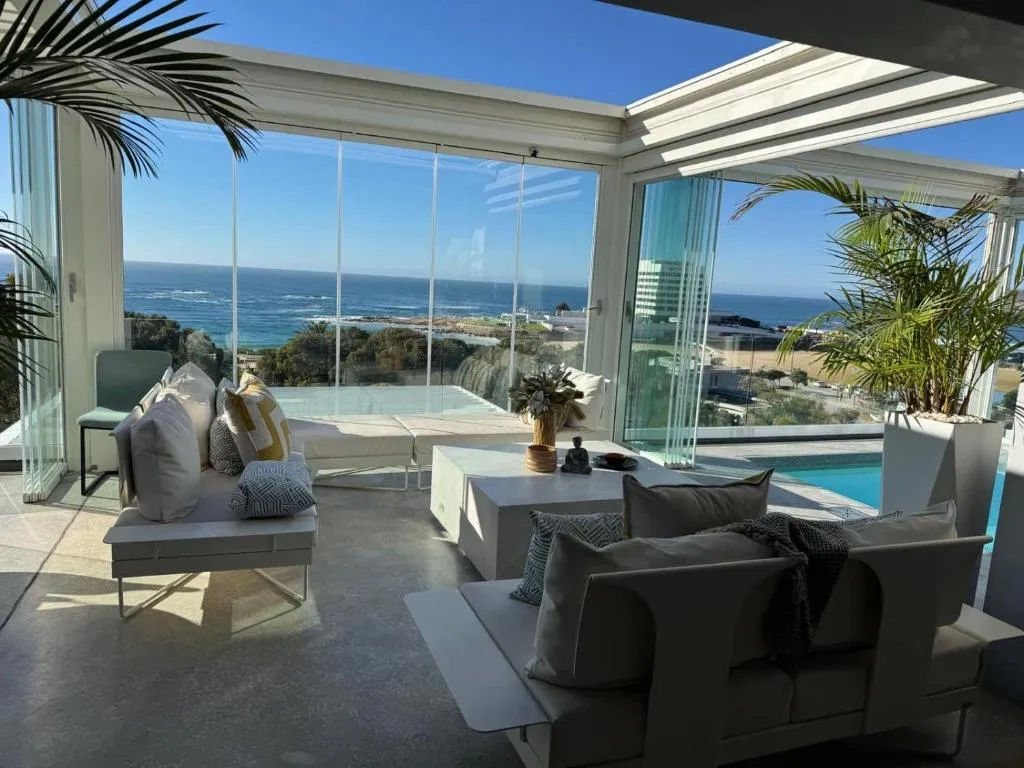 Glass-walled sunroom lounge with daybeds overlooking the pool and open ocean