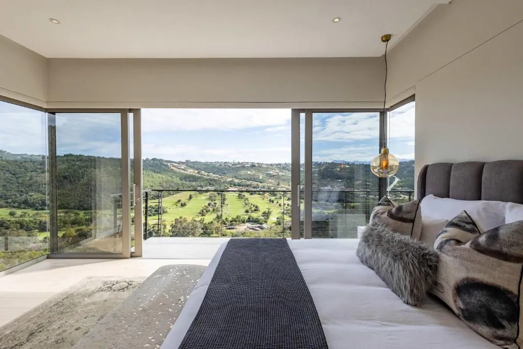 Bedroom with corner glass doors opening onto a balcony overlooking green hills and golf course