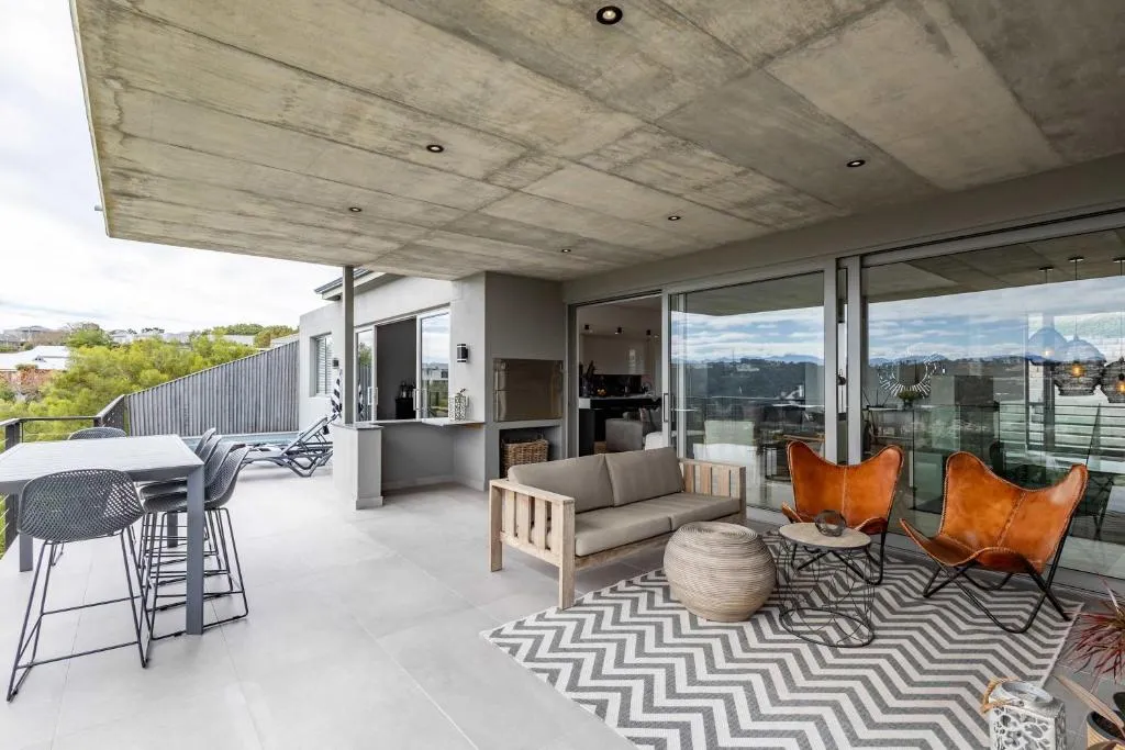 Covered patio with a built-in braai, dining table and leather butterfly chairs overlooking wooded hills