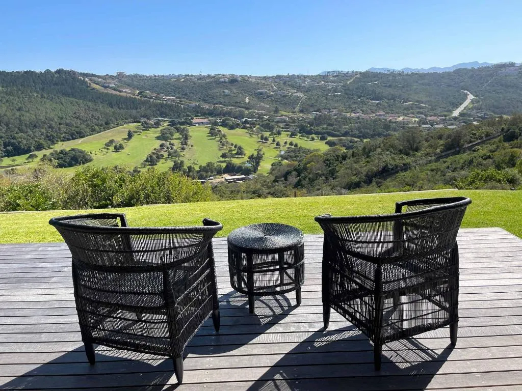 Wicker chairs on a wooden deck facing a sweeping view over green hills and a golf course