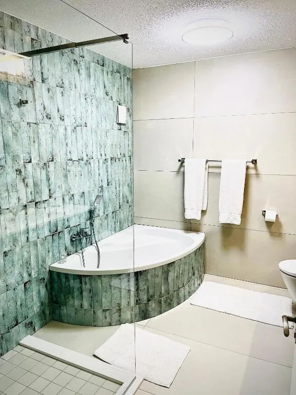 Bathroom with a corner tub, glass shower screen and green tiled feature wall