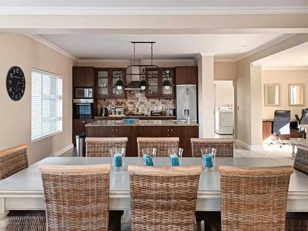 Dining table for eight in wicker chairs beside an open kitchen with dark wood cabinetry