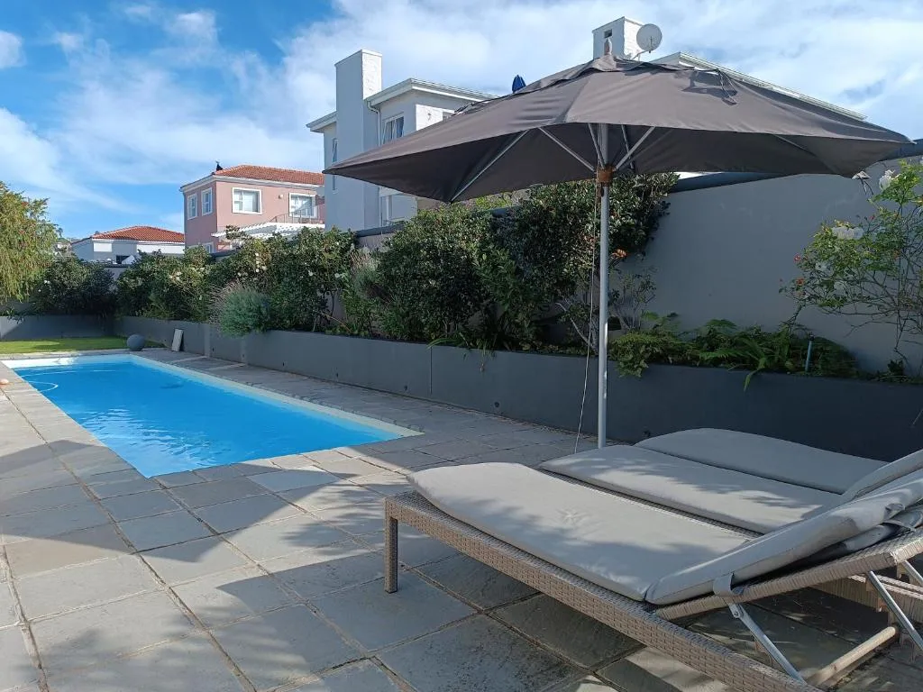 Walled garden pool with loungers and an umbrella, bordered by rose bushes and a stone patio