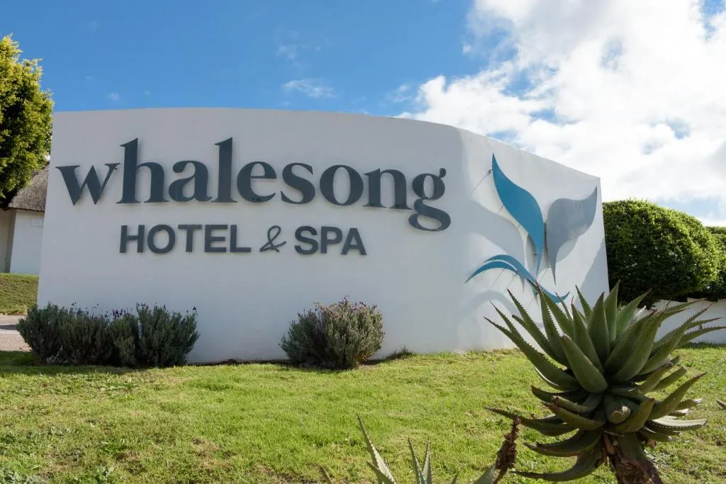 Whalesong Hotel & Spa entrance signage with its whale-tail logo among aloes