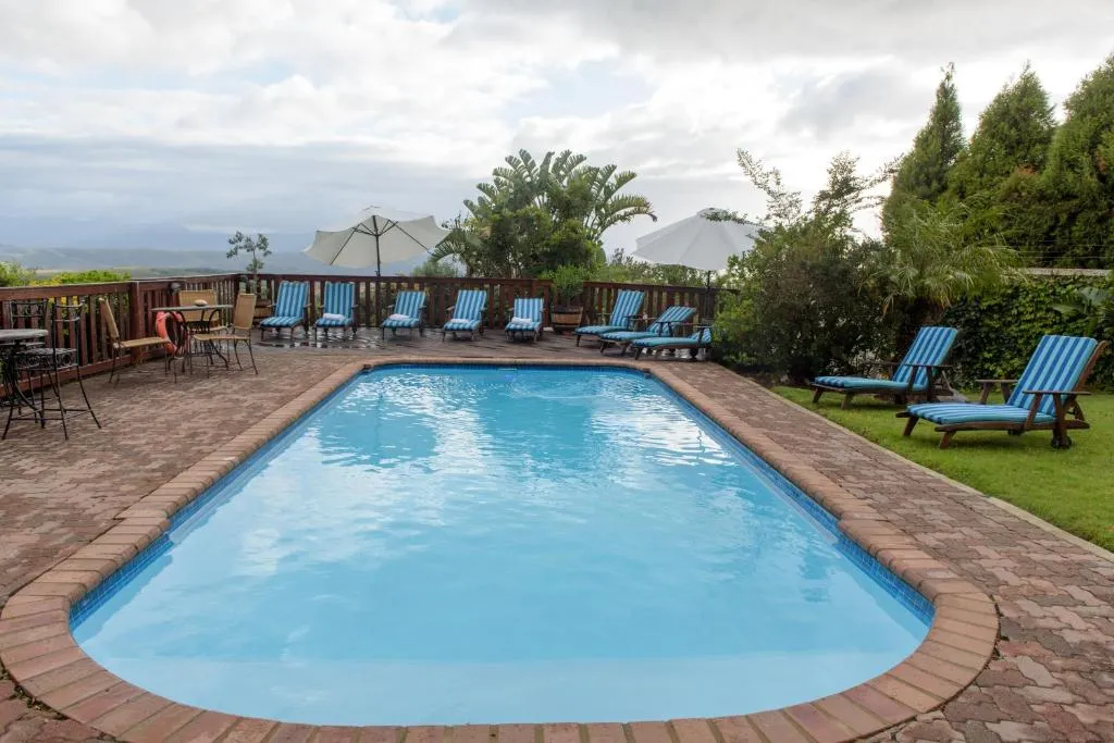 Swimming pool deck with striped loungers, umbrellas and hills in the distance