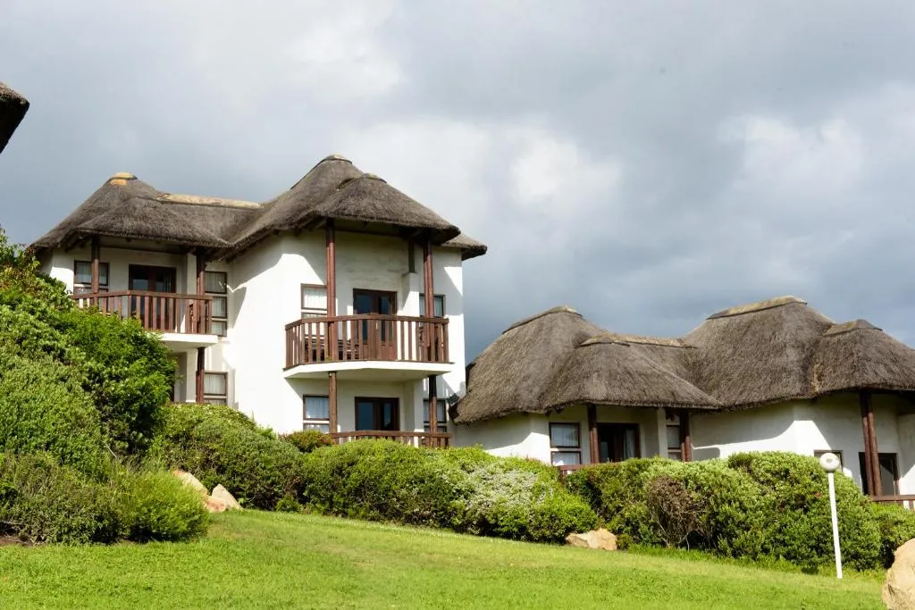Thatched double-storey hotel building with wraparound balconies set among a coastal garden