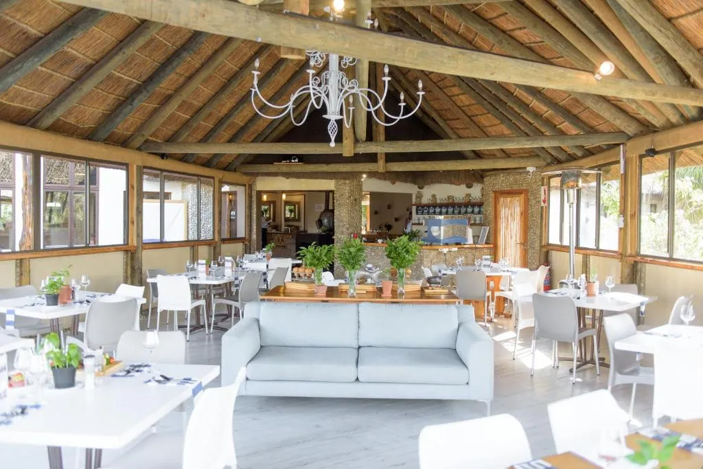 Thatched-roof restaurant with a chandelier, timber beams and tables set for dining