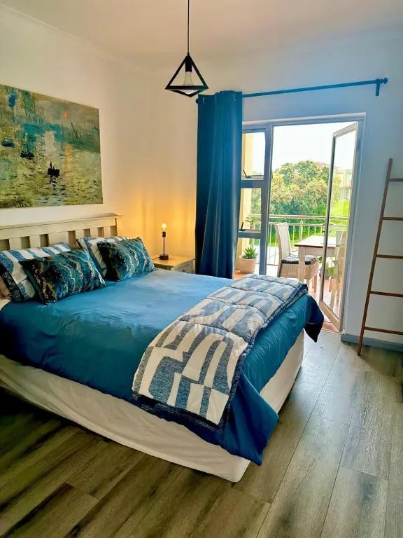 Bedroom with a teal bedspread, patterned artwork, and glass doors opening onto a garden-facing balcony