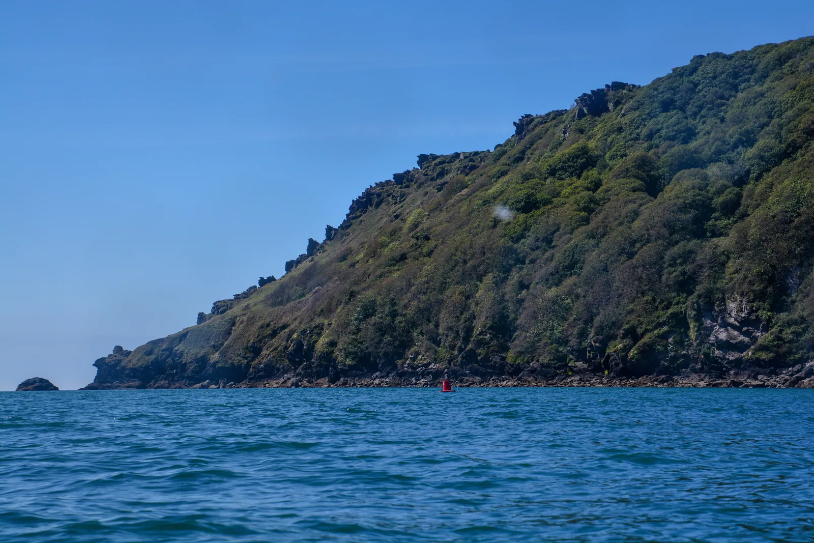 The rocky, wooded headland at Bolt Head near Salcombe seen from the water, with a navigation buoy off the point