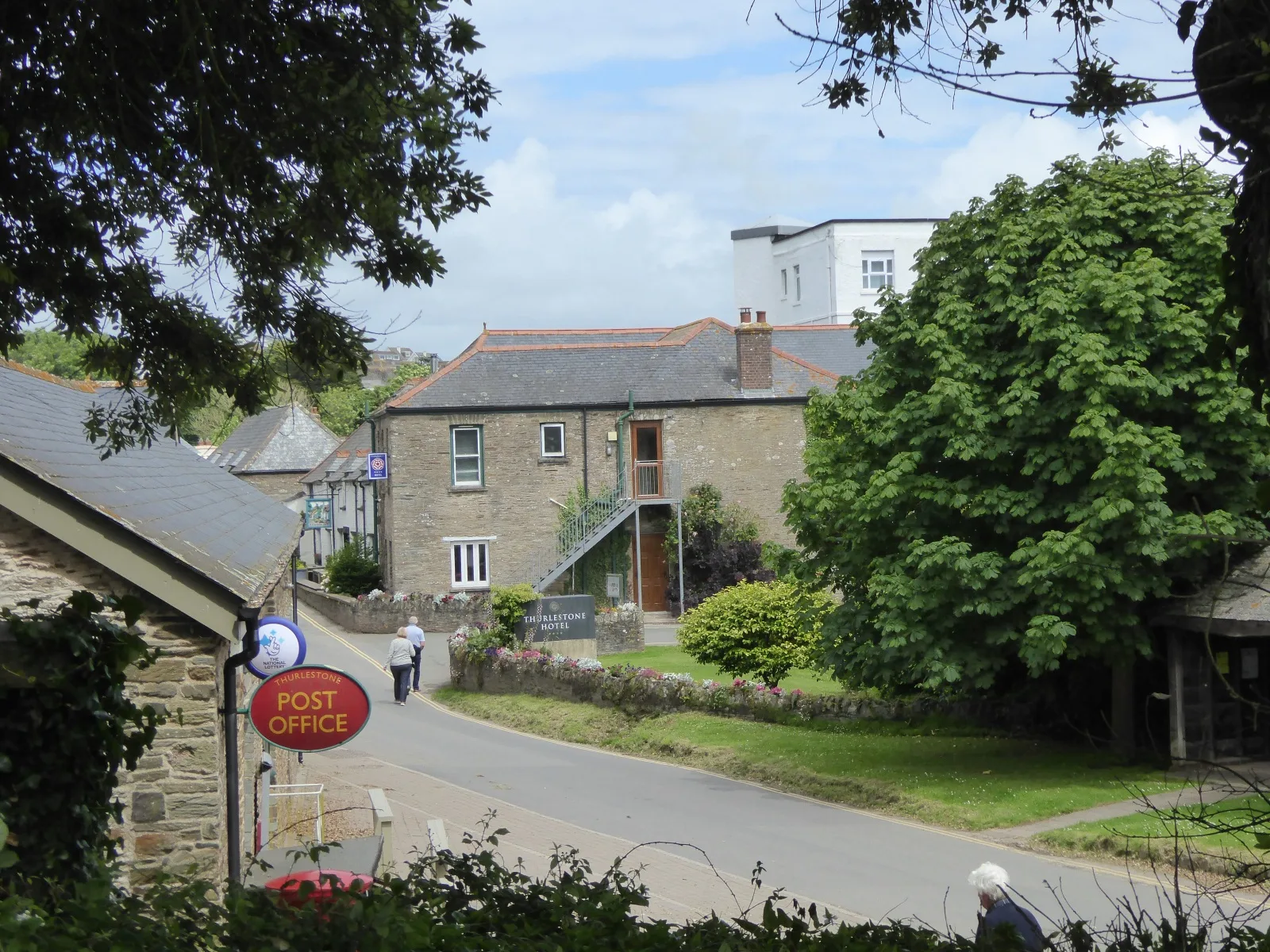 The road through Thurlestone village, with the Thurlestone Hotel name board on a low wall and the hotel's stone and white buildings behind