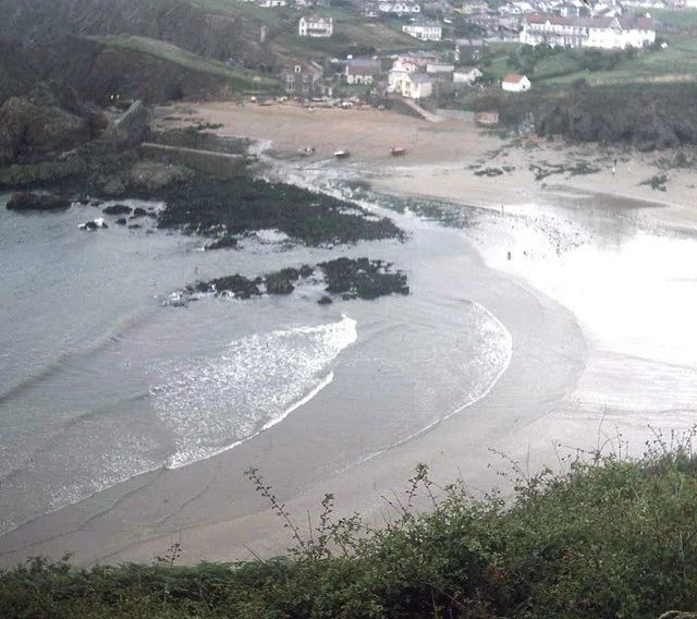 Hope Cove seen from the coast path above, with the harbour wall and slipway at Inner Hope in the foreground and sand running north towards the houses of Outer Hope