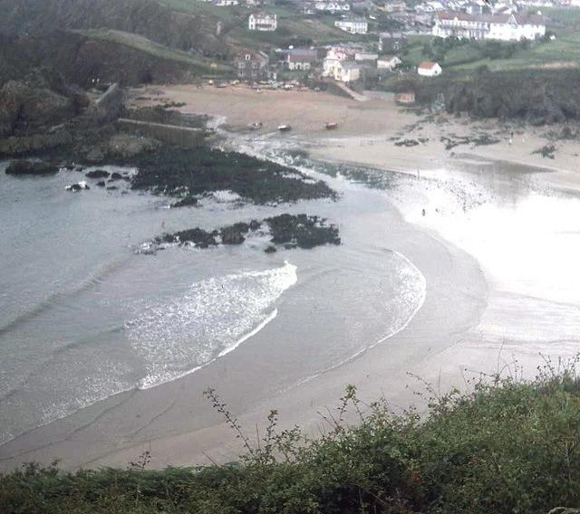 Hope Cove seen from the coast path above, with the harbour wall and slipway at Inner Hope in the foreground and sand running north towards the houses of Outer Hope