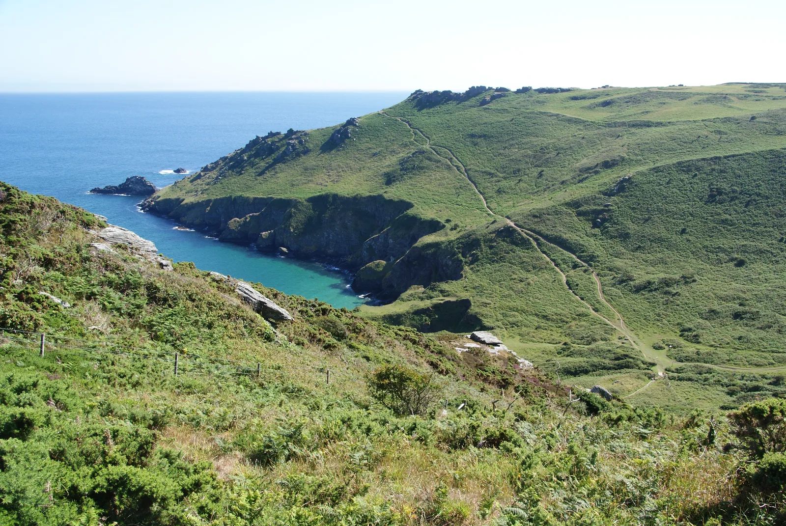 The South West Coast Path crossing green clifftop grassland towards Bolt Head near Salcombe, with a sheltered rocky cove of turquoise water below