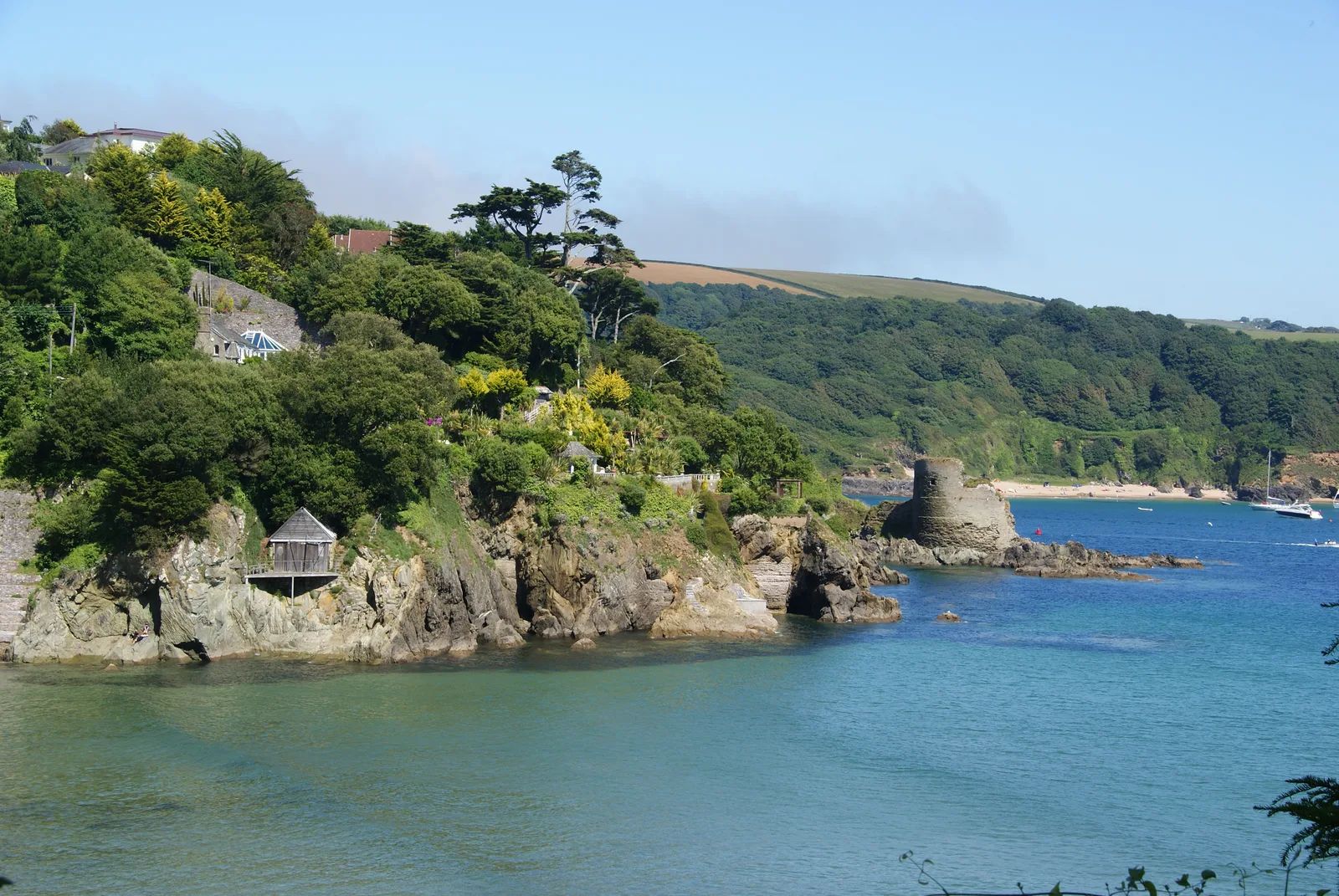 The ruined semicircular tower of Fort Charles on a rocky outcrop at North Sands, Salcombe, with wooded hillside behind