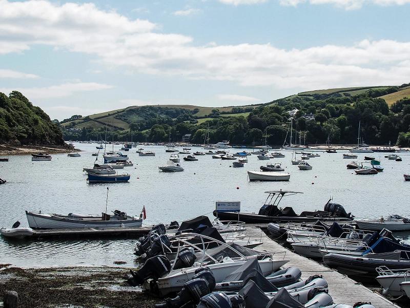 Moorings in Batson Creek at Salcombe, with dinghies and small motorboats drawn up on a pontoon in the foreground and moored boats on the water beyond, green hills rising behind