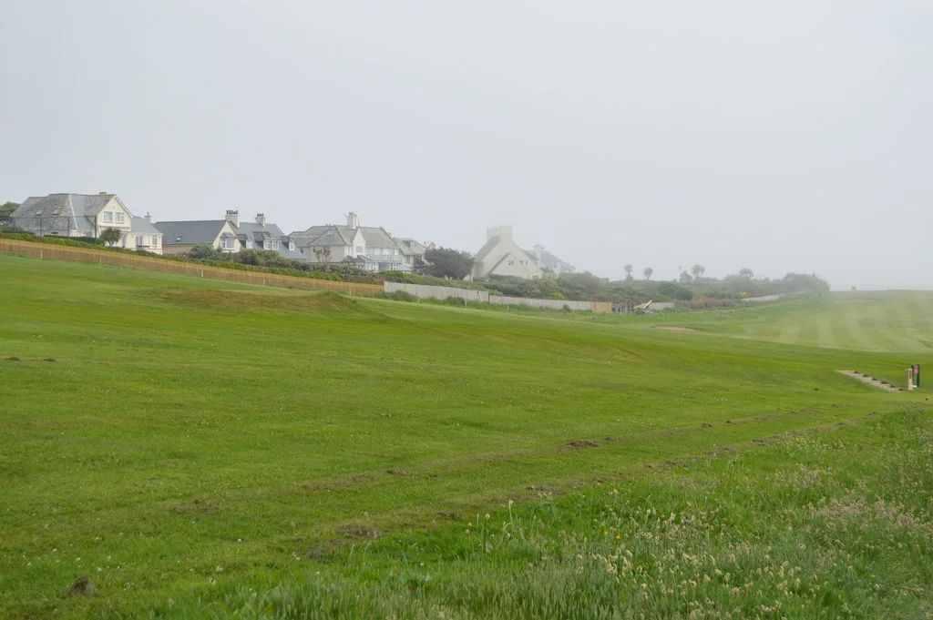Houses in Thurlestone village seen across a stretch of golf course grass on a hazy, overcast day