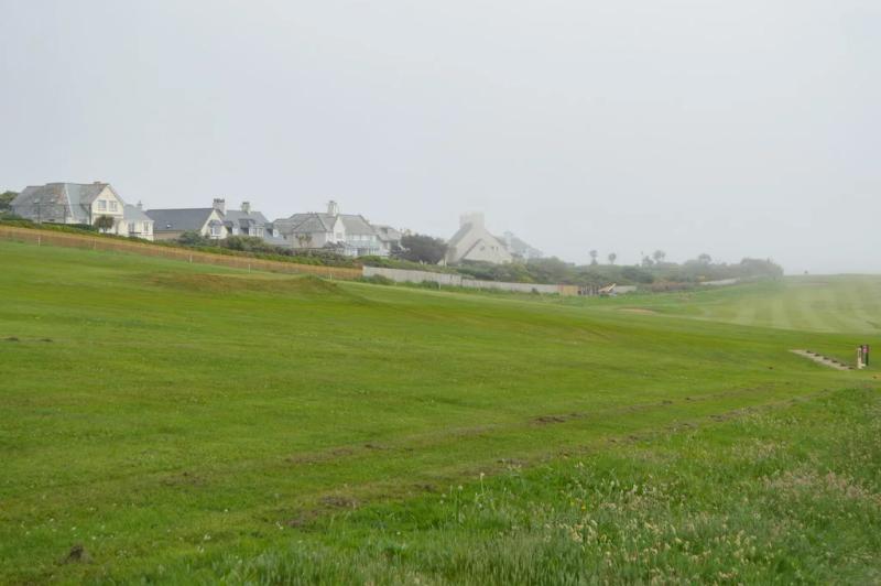 Houses in Thurlestone village seen across a stretch of golf course grass on a hazy, overcast day